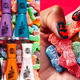 Left: Nail polish in seven colors on a bed of Sour Patch Kids candies. Right: A manicured hand holding Sour Patch Kids candies.